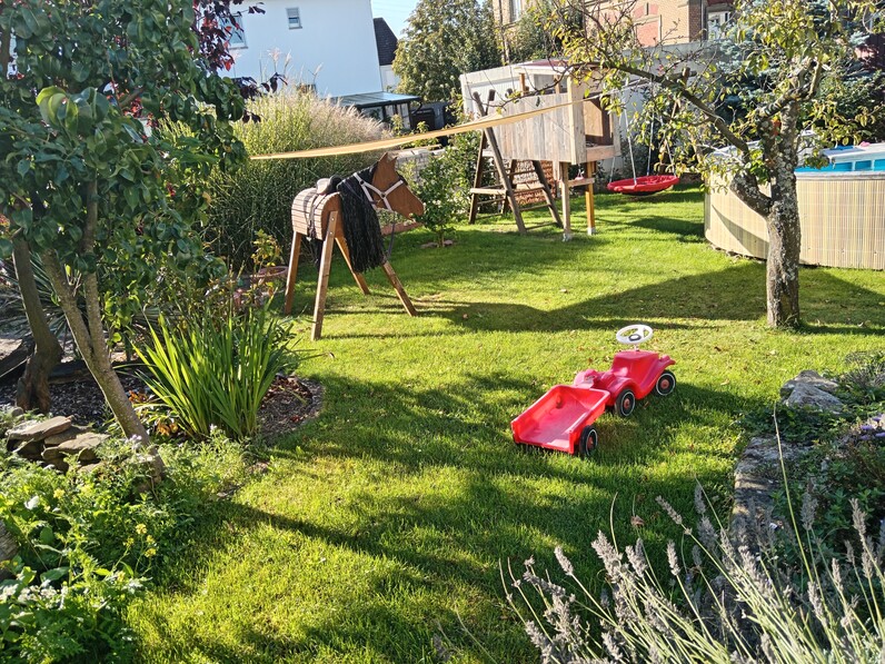 Bild: Garten mit Rasenfläche und Beeten, Spielzeug und Bäumen.